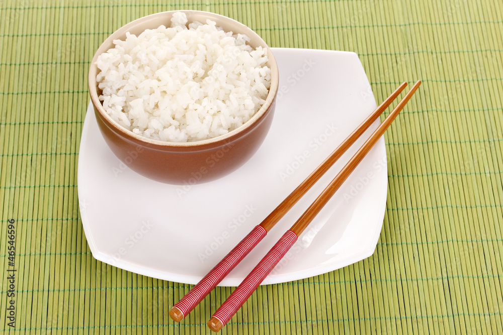 Bowl of rice and chopsticks on plate on bamboo mat