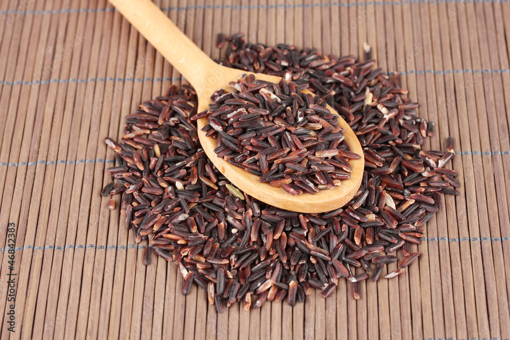 black rice  in wooden  spoon on bamboo mat