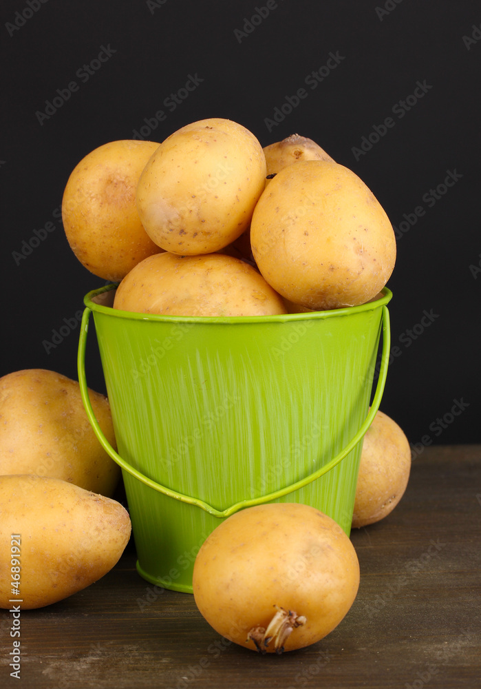 Ripe potatoes in pail on wooden table on black background