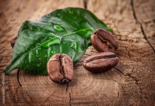 Fototapeta na wymiar Coffee grains and green leaf on grunge wooden background