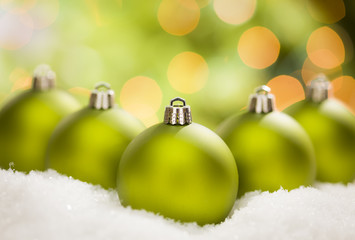 Green Christmas Ornaments on Snow Over an Abstract Background