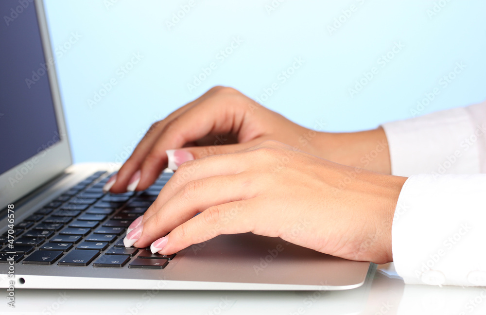 Hands typing on laptop keyboard close up on  blue background