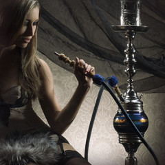 Wall Mural - A young blond woman smoking a hookah on a silk background