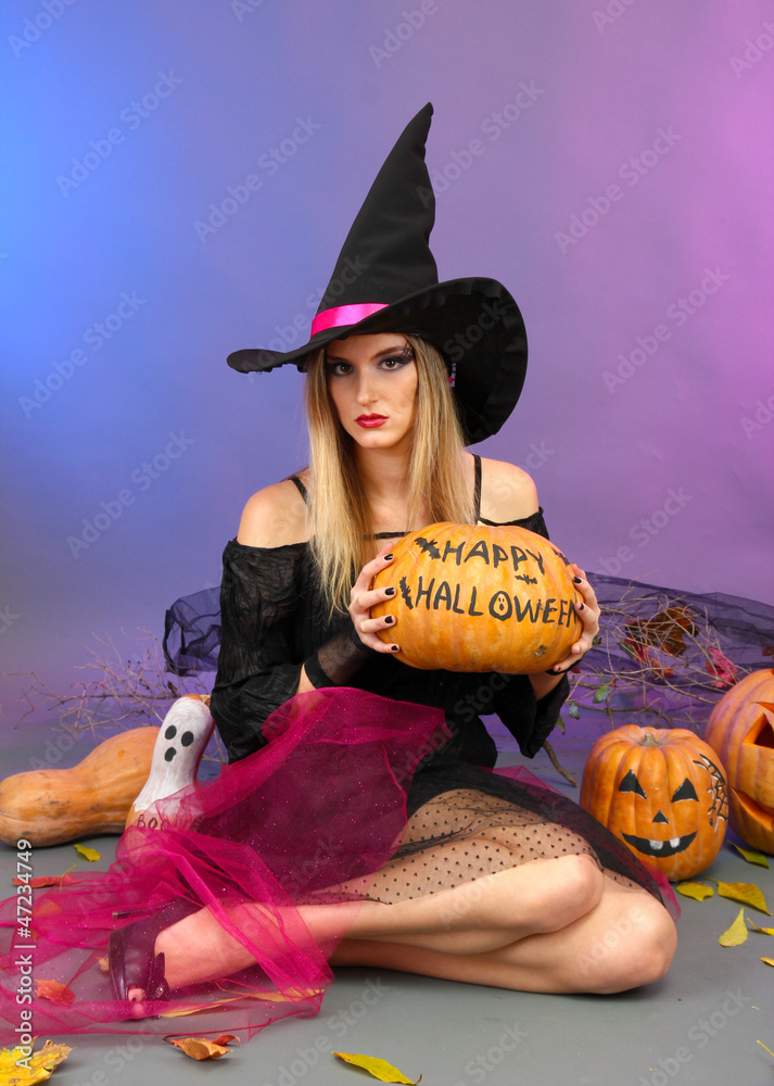 Halloween witch holding pumpkin on color background
