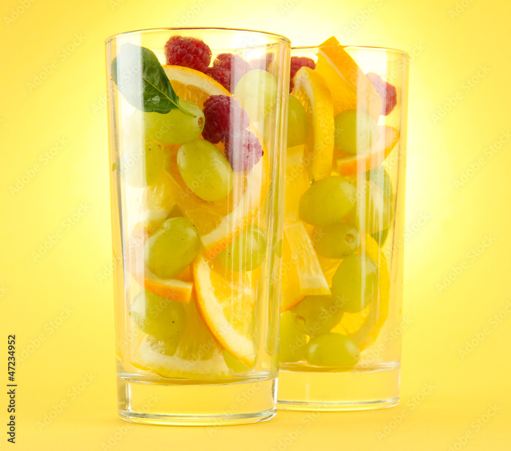 transparent glasses with citrus fruits, on yellow background