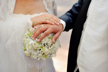 Close-up hands of bride and groom on a bouquet of flowers