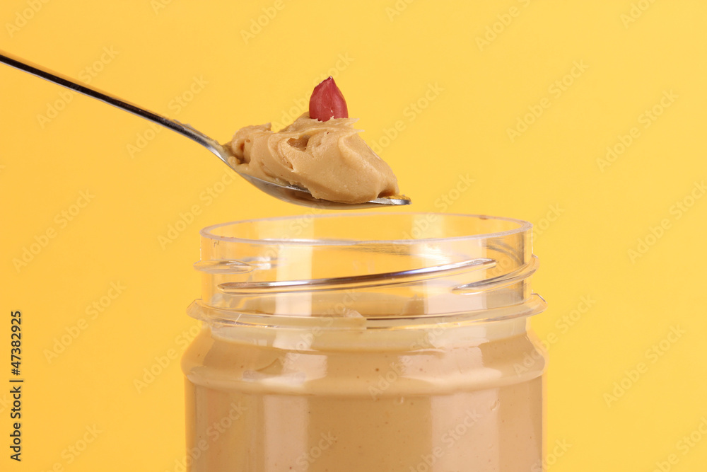 Delicious peanut butter in jar and spoon on yellow background