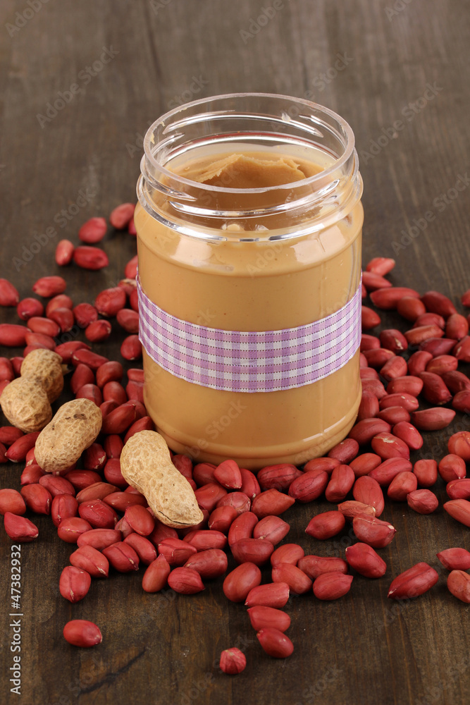 Delicious peanut butter in jar on wooden table close-up