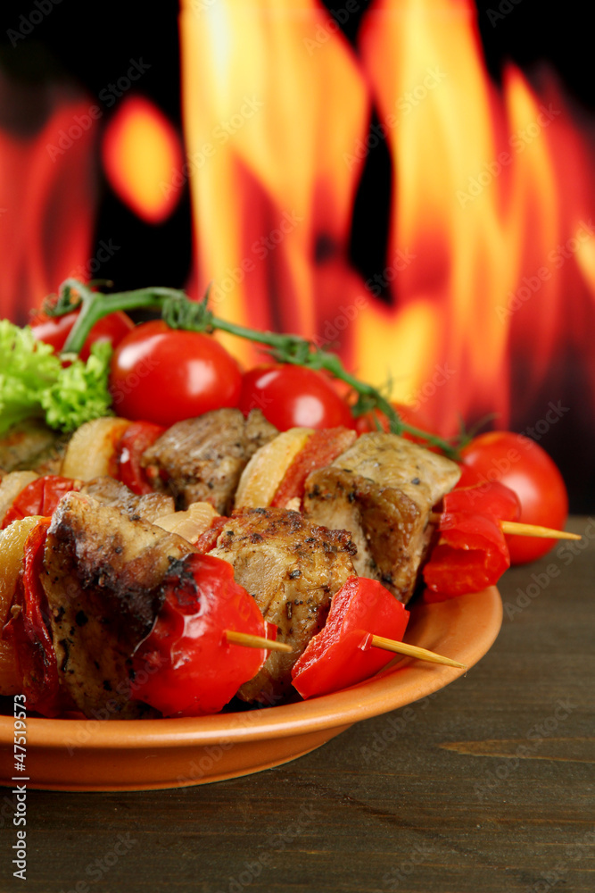 tasty grilled meat and vegetables on plate, on fire background