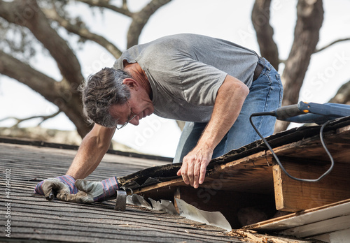 Fotografie, Obraz Man Examining and Repairing Rotten Leaking House Roof