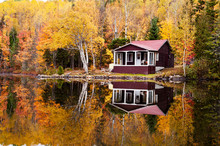 Reflections Of A Autumn Forest And A House In A Lake