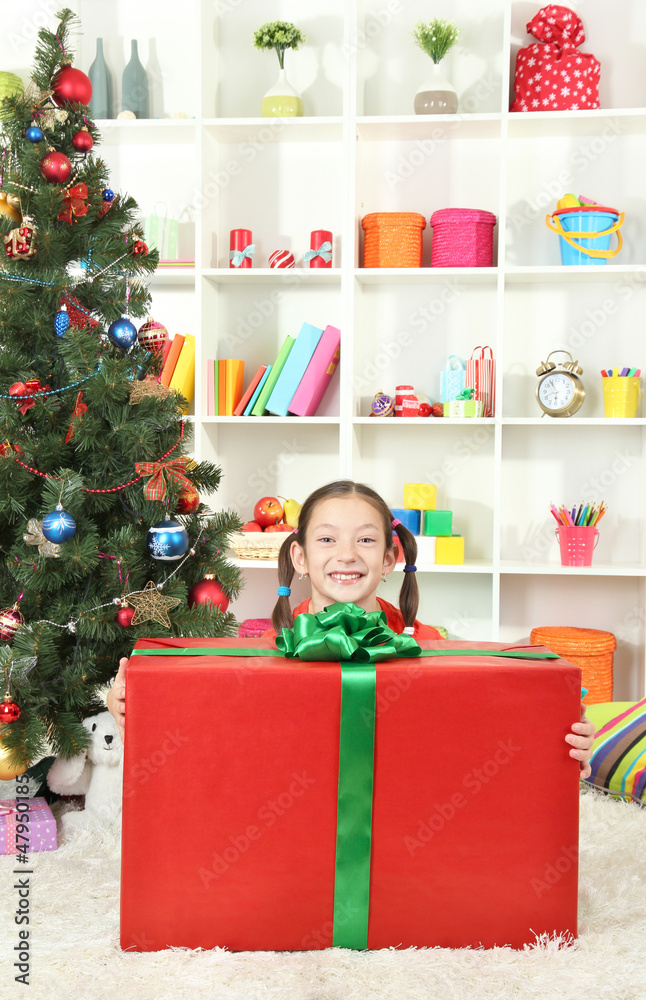 Little girl with large gift box near christmas tree