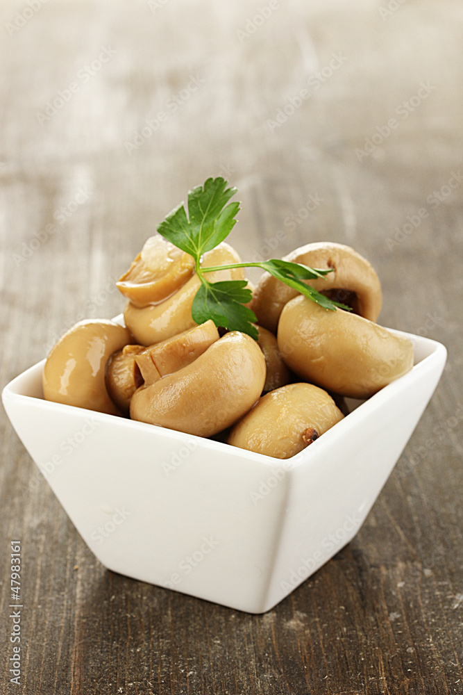 Delicious marinated mushrooms in bowl on wooden table close-up