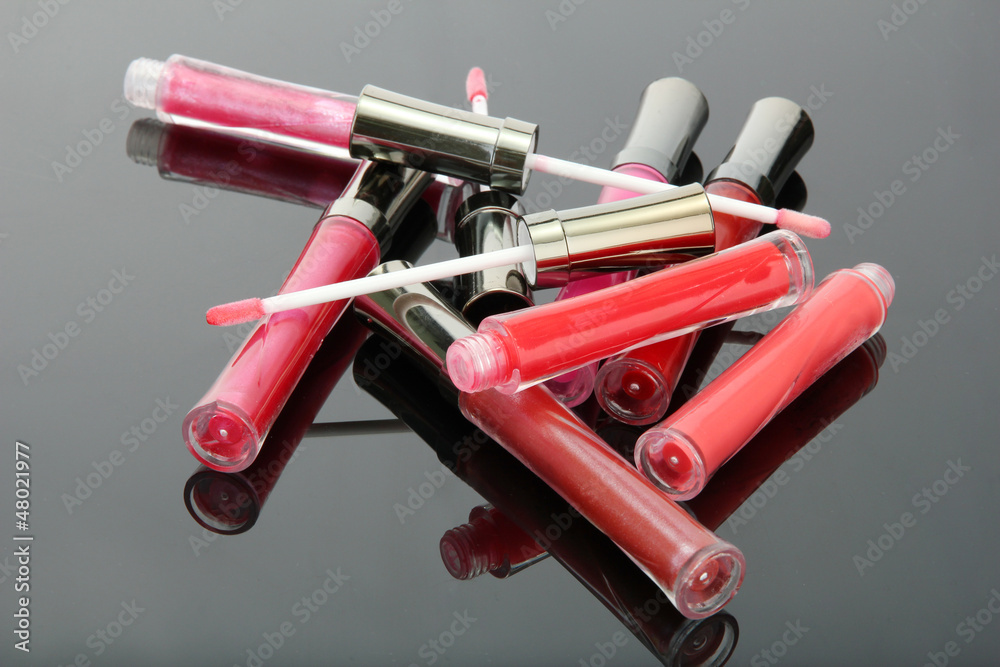 beautiful lip glosses with rose petals, on grey background
