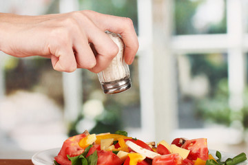 Hand adding salt using  salt shaker on bright background