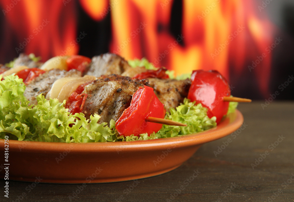 tasty grilled meat and vegetables on plate, on fire background