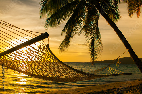 Naklejka ścienna Hammock silhouette with palm trees on a beach at sunset