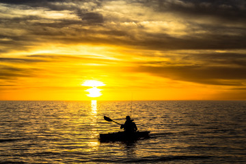 Fisherman in the kayak on the ocean in front of dramatic sunset