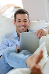 Cheerful young man laying in sofa with digital tablet