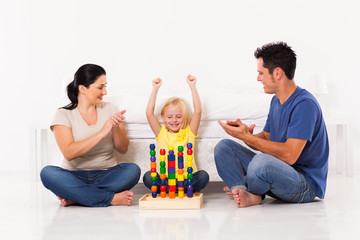 happy little girl playing toys with parents on bedroom floor