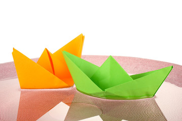 Color paper ship in water on pink plate, close-up