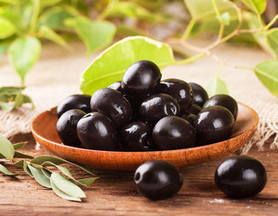 Black olives in a wooden plate and a rough board