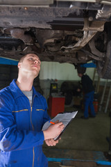 Poster - Mechanic under car writing on clipboard