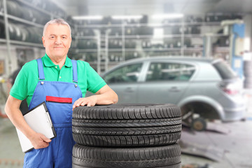 Wall Mural - Mature mechanic posing on a tires in front of car at repair shop