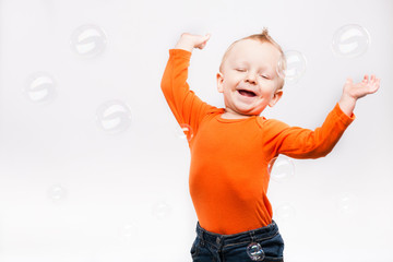 Photo of little boy onlight grey background, playing with soap b