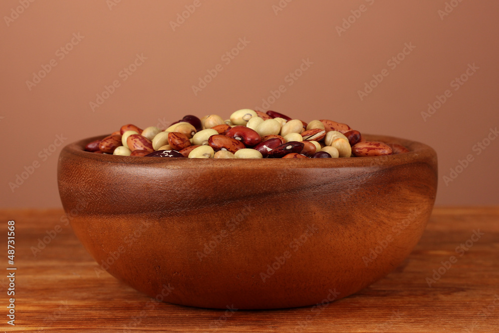 Wooden bowl with beans on wooden table on brown background