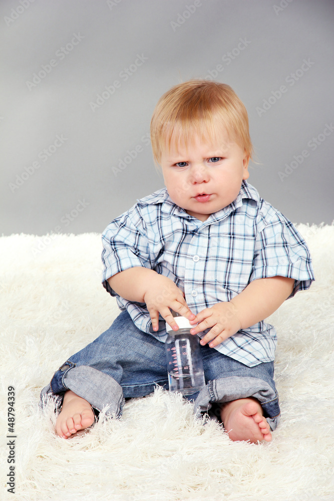 Little boy sitting on white carpet on gray background