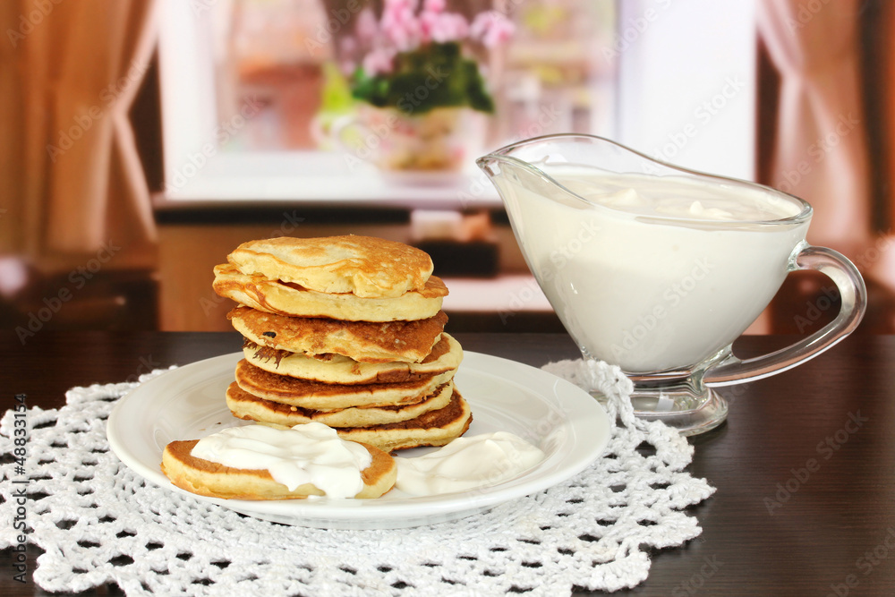 Sweet pancakes on plate with sour cream on table in room