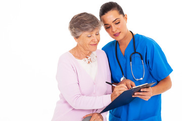 senior woman signing medical form with help from nurse