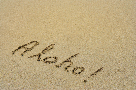 Aloha handwritten in sand on a beach