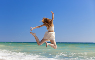 Young redhead girl jumping at the beach.