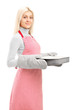 Young woman wearing cooking mittens and apron holding a baking t