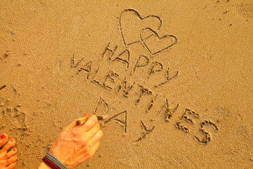 Wall Mural - Female hand writing on the sand beach: Happy Valentine's Day