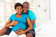 happy expecting african american couple sitting on bed at home