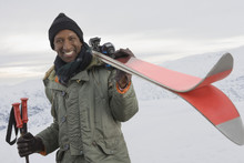 Mixed Race Man Carrying Skis On Snowy Slope