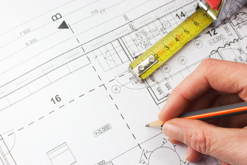 Plan of a house, ruler and a hand writing with a pencil