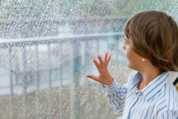 Smiling boy watching the rain outside at a window