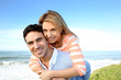 © goodluz - Man giving piggyback ride to girlfriend by the sea