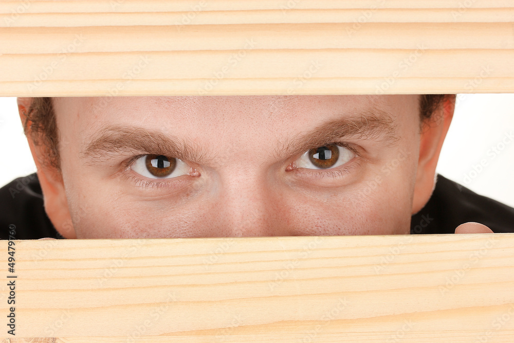 Man eyes looking through hole in wooden desk