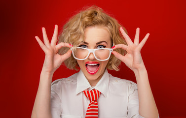 Surprised woman looking you above eyeglasses, isolated on red