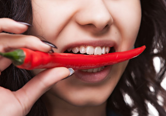 woman holding red hot chili pepper in mouth