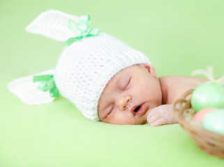 Fototapete - funny newborn baby dressed in Easter bunny cap with eggs