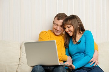 Smiling man and woman with laptop sitting on sofa