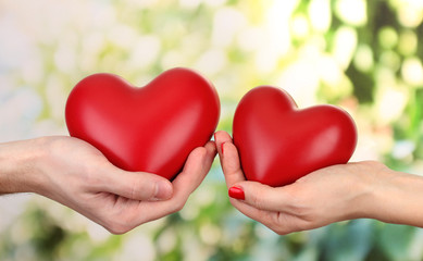 Red hearts in woman and man hands, on green background