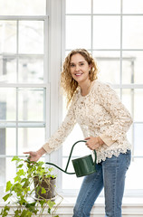 Smiling woman watering plant at home