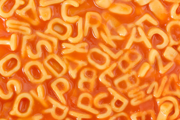 Background of pasta shaped alphabet letters in tomato sauce
